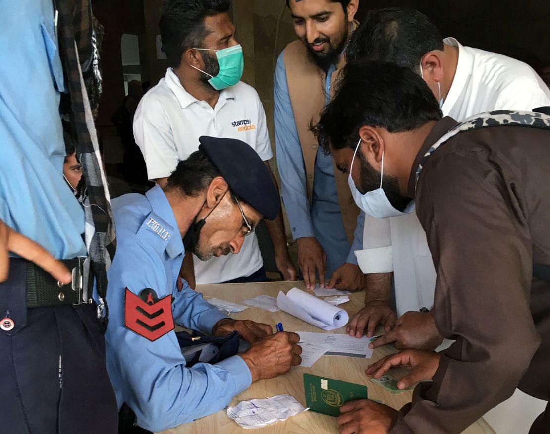 A police officer helps men to fill out forms to obtain a coronavirus vaccine, so they can travel to work abroad, at a mass vaccination centre in Islamabad, Pakistan on June 28, 2021. 