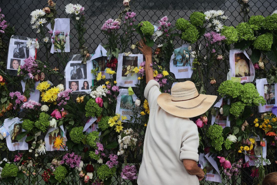 A person adds flowers Monday to a memorial that has pictures of some of the missing from the partially collapsed Champlain Towers South condo building in Surfside.
