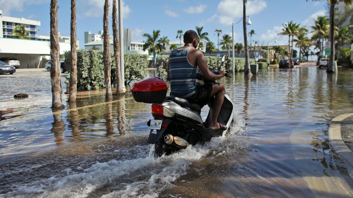 A man on a motorbike navigates through high-tide flooding in Hollywood, Florida, north of Miami.