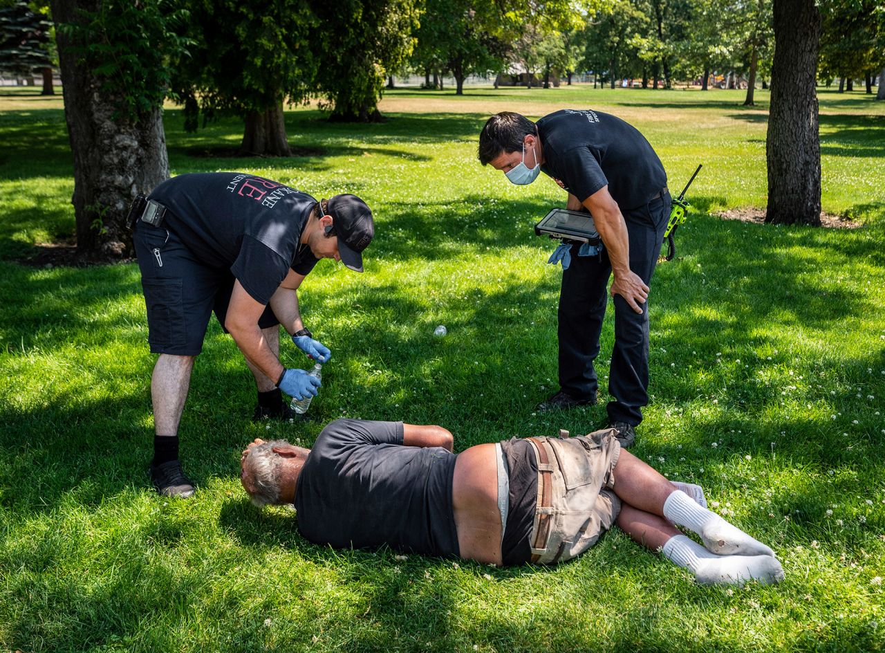 Firefighters check on a man in Spokane's Mission Park on Tuesday.