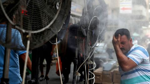 A man stands by fans spraying mist along a street in Iraq's capital, Baghdad, on June 30.