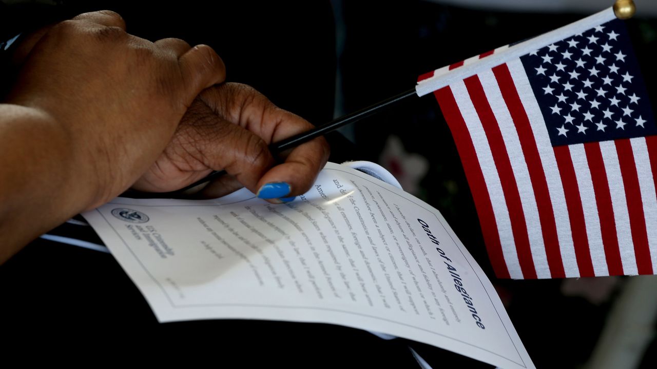 An immigrant holds a flag and the Oath of Allegiance during a US ceremony for naturalized citizens aboard the battleship USS Iowa in the Port of Los Angeles on Thursday, July 1, 2021.