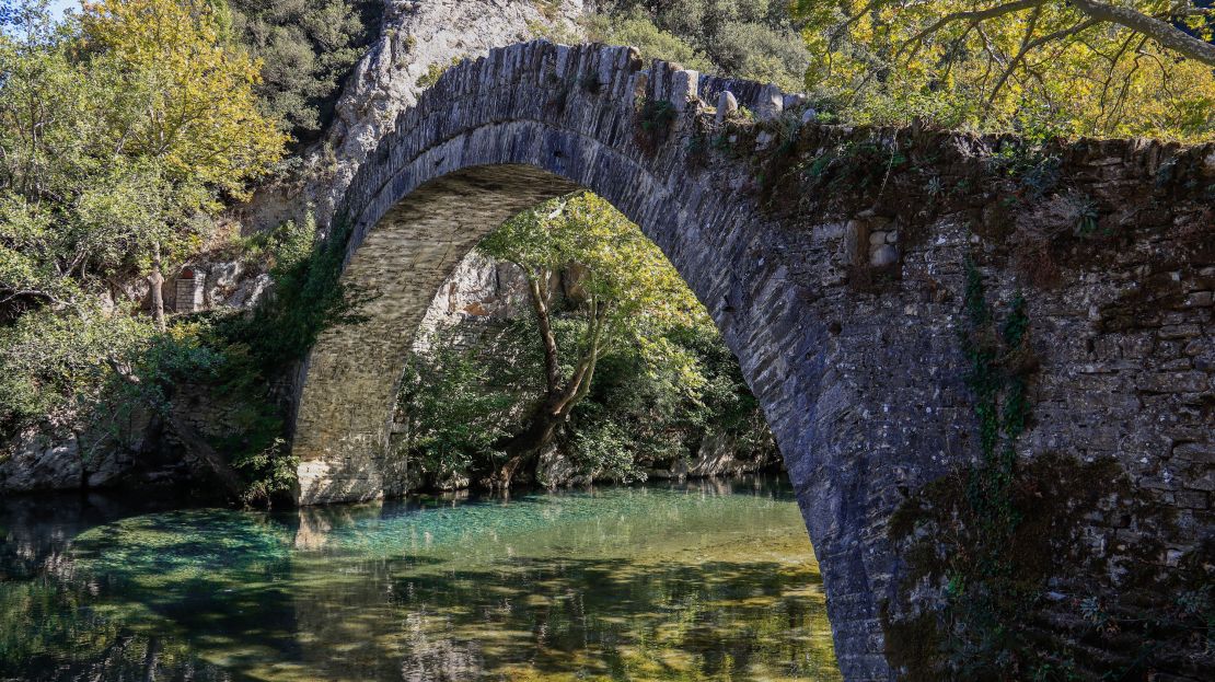 An old stone bridge spans the Voidomatis River.