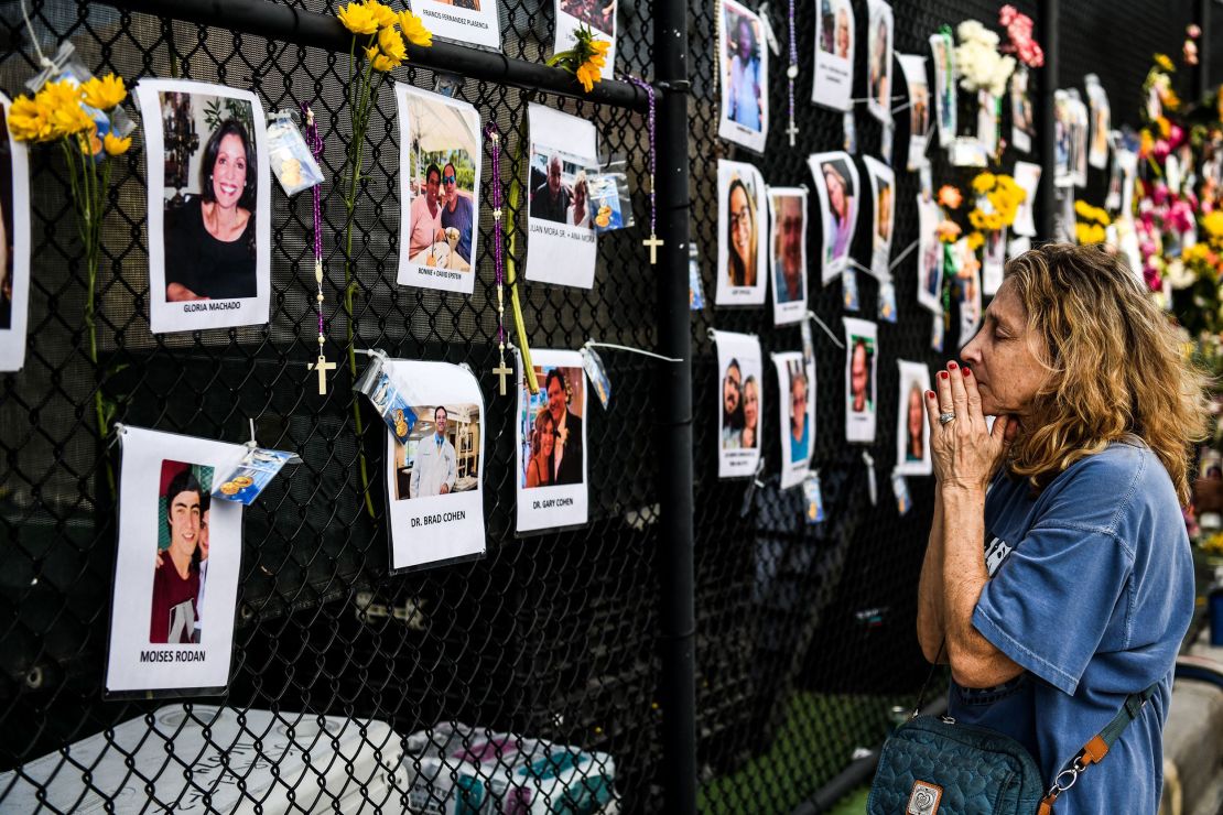 A woman prays in front of photos at the makeshift memorial for the victims of the building collapse, near the site of the accident in Surfside, Florida on June 27, 2021.