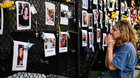 A woman prays in front of photos at the makeshift memorial for the victims of the building collapse, near the site of the accident in Surfside, Florida on June 27, 2021. 