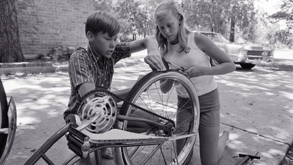 Jan Aldrin and her older brother Mike work on repairing Jan's bike tire, which she punctured with a tack. Despite their father landing on the moon, much of life back home still went on as usual.