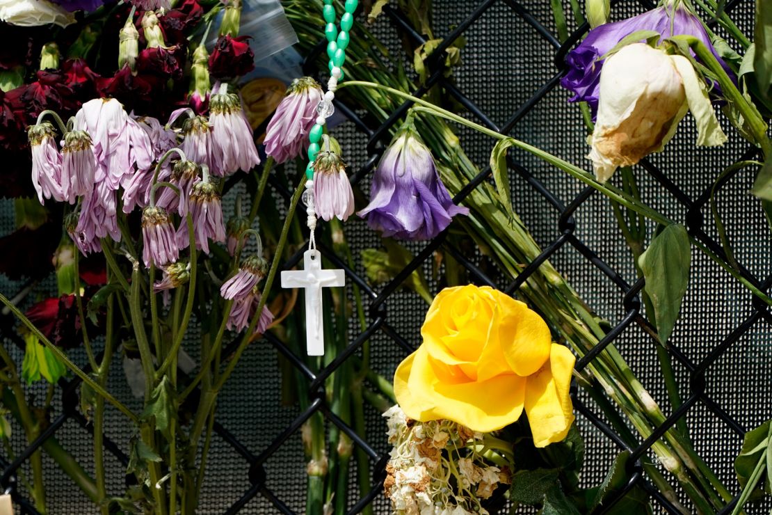 A cross hangs among wilting flowers at a makeshift memorial near Champlain Towers South.