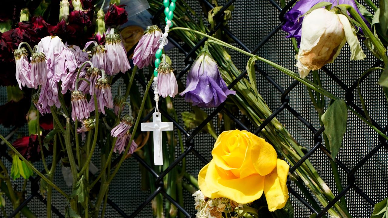 A cross hangs among wilting flowers at a makeshift memorial near Champlain Towers South.