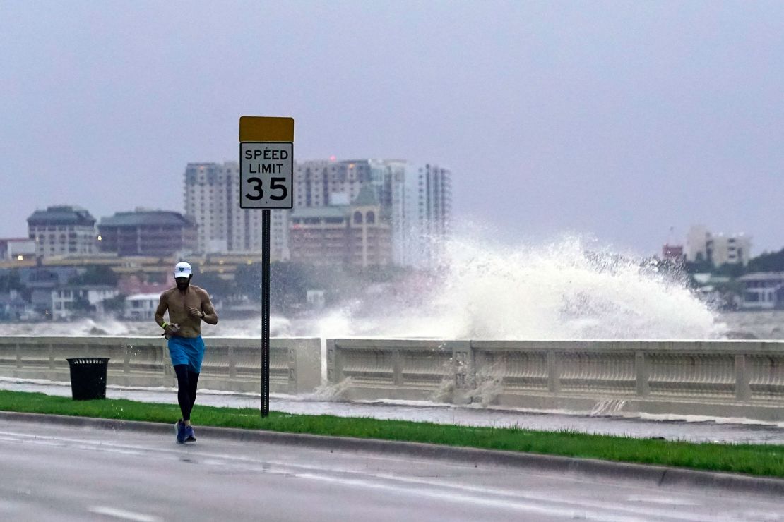 A jogger runs Wednesday in Tampa as a wave breaks over a seawall.