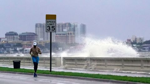 A jogger runs Wednesday in Tampa as a wave breaks over a seawall.