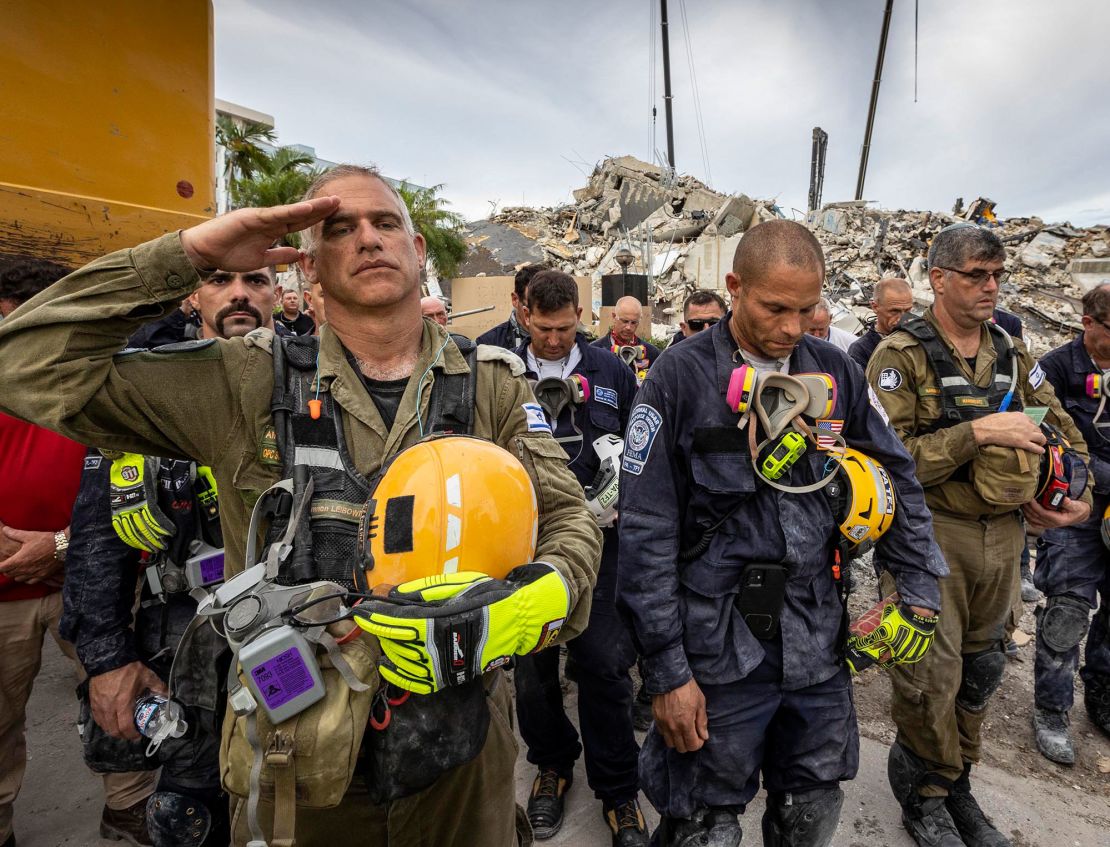 Members of search and rescue teams gather for a moment of silence and prayer at the memorial to the victims in the collapsed 12-story Champlain Towers South condo building.