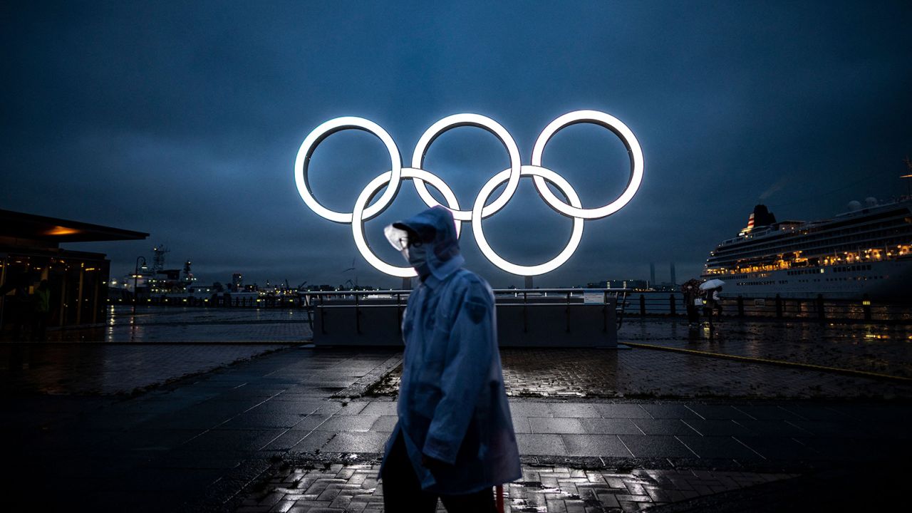 TOPSHOT - A man walks past the Olympic Rings lit up at dusk in Yokohama on July 2, 2021. (Photo by Philip FONG / AFP) (Photo by PHILIP FONG/AFP via Getty Images)