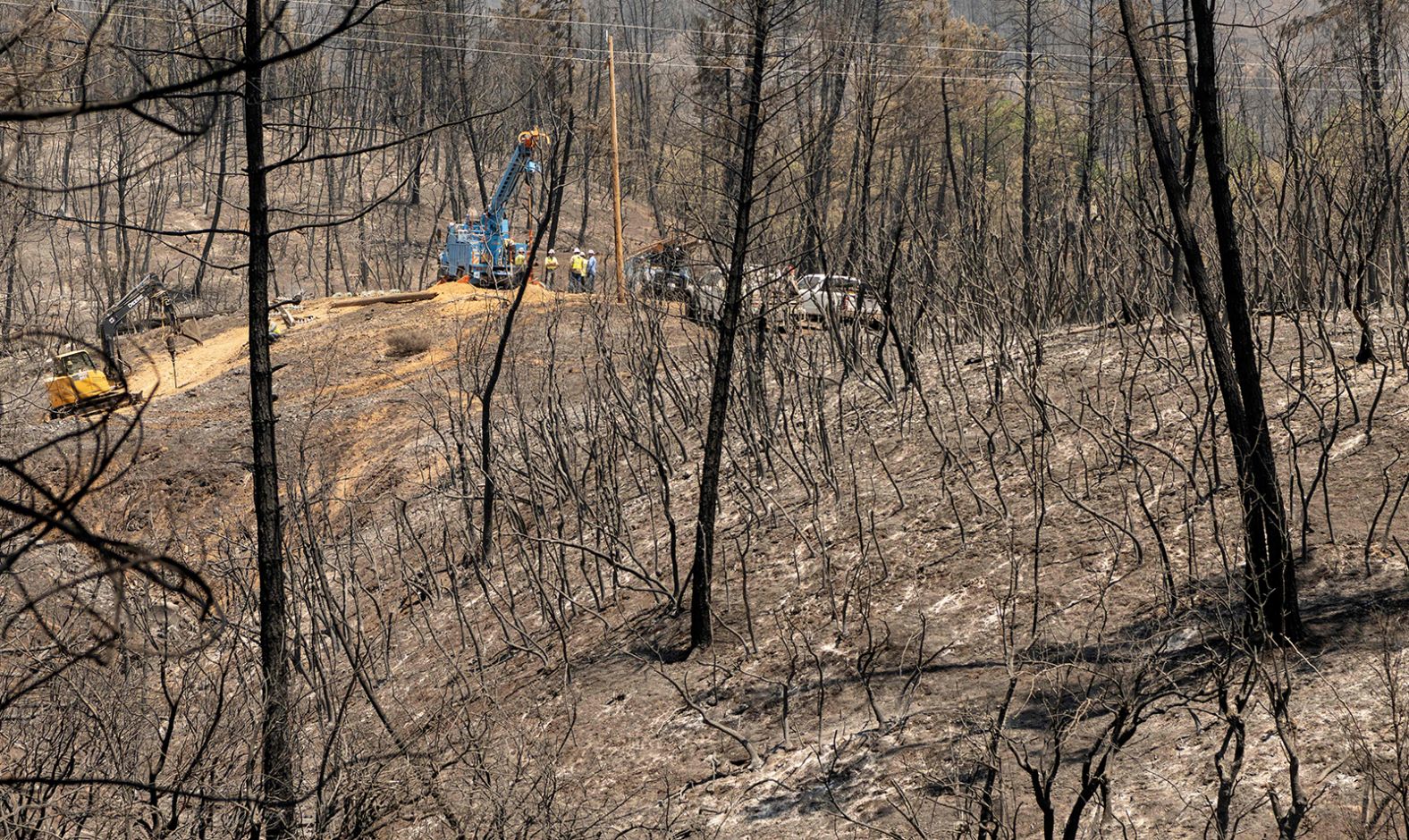 A utility crew works on power lines in July 2021, in front of a hillside that was burned by the Salt Fire in California's Shasta County.