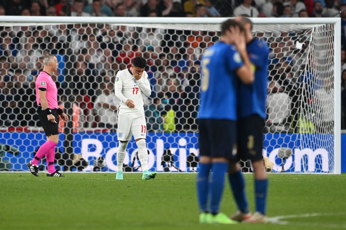 Manuel Locatelli and Giorgio Chiellini of Italy celebrate as Jadon Sancho looks dejected after missing England's fourth penalty.
