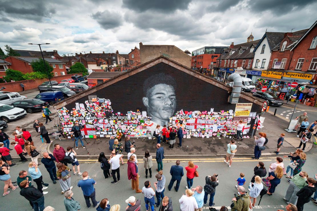 People look at the messages of support and the newly repaired mural of Rashford.