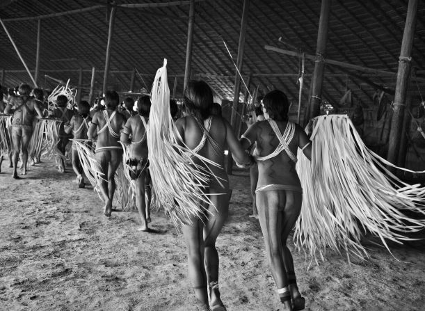 Visitors dance upon arrival to the Piaú community, Yanomami Indigenous Territory, 2019. Dancing in a circle they present themselves to locals, the men enacting an "invasion" by pretending to shoot arrows, before everyone heads outside for conversation, Salgado writes.