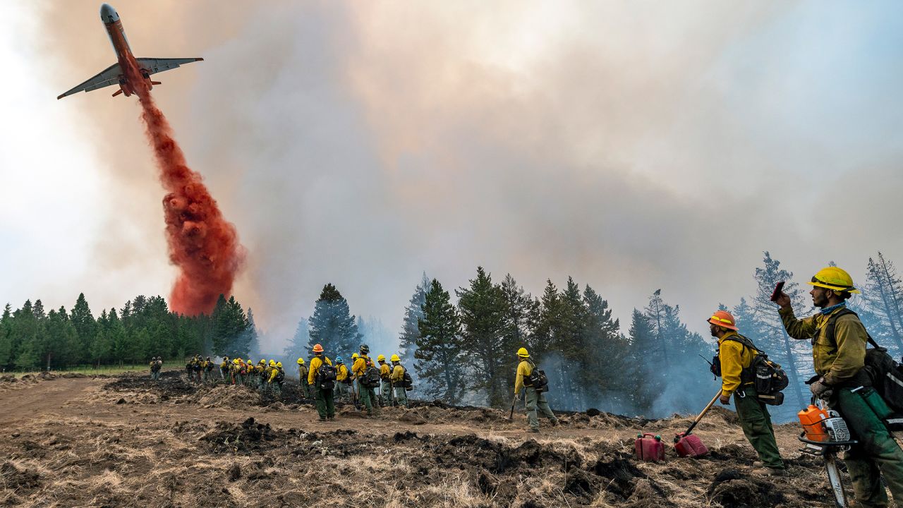 Wildland firefighters watch and take video with their cell phones as a plane drops fire retardant Monday on Harlow Ridge above the Lick Creek Fire, southwest of Asotin, Washington.