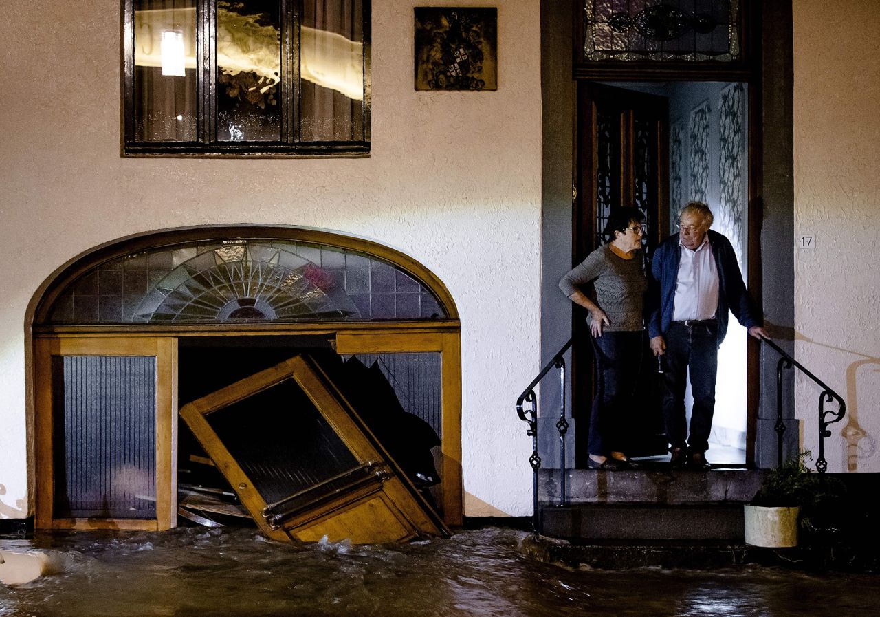 A man and woman stand on the stoop of their home as they look at floodwaters in Geulle, Netherlands.