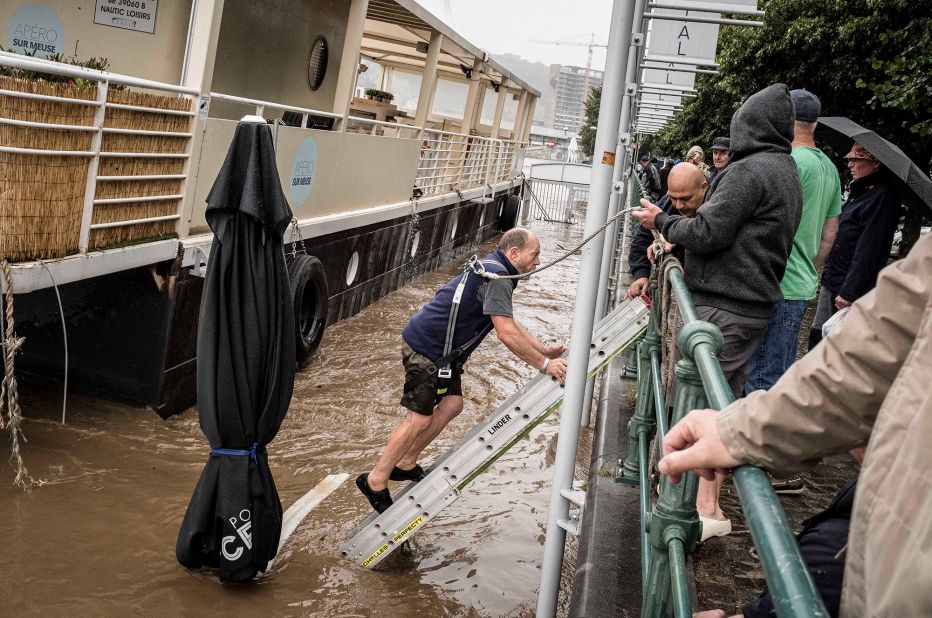 A man steps down a ladder in an attempt to cut his boat loose in the Meuse River in Liege, Belgium.