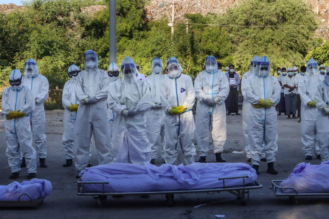 Volunteers wearing personal protective equipment (PPE) pray in front of bodies of people who died from  Covid-19 during their funeral at a cemetery in Mandalay on July 14.