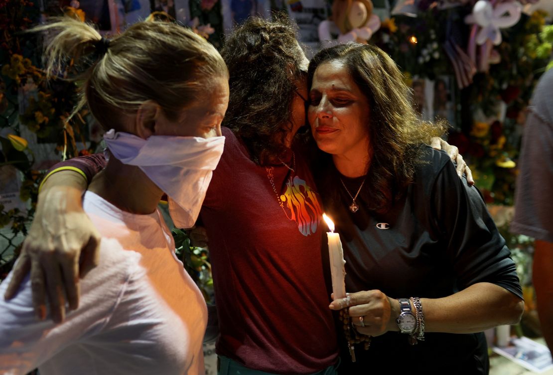 Michelle D'Antuono, Dana Kulvin, and Soraya Batista hug as they visit the memorial that has pictures of some of the victims from the partially collapsed 12-story Champlain Towers South condo building.