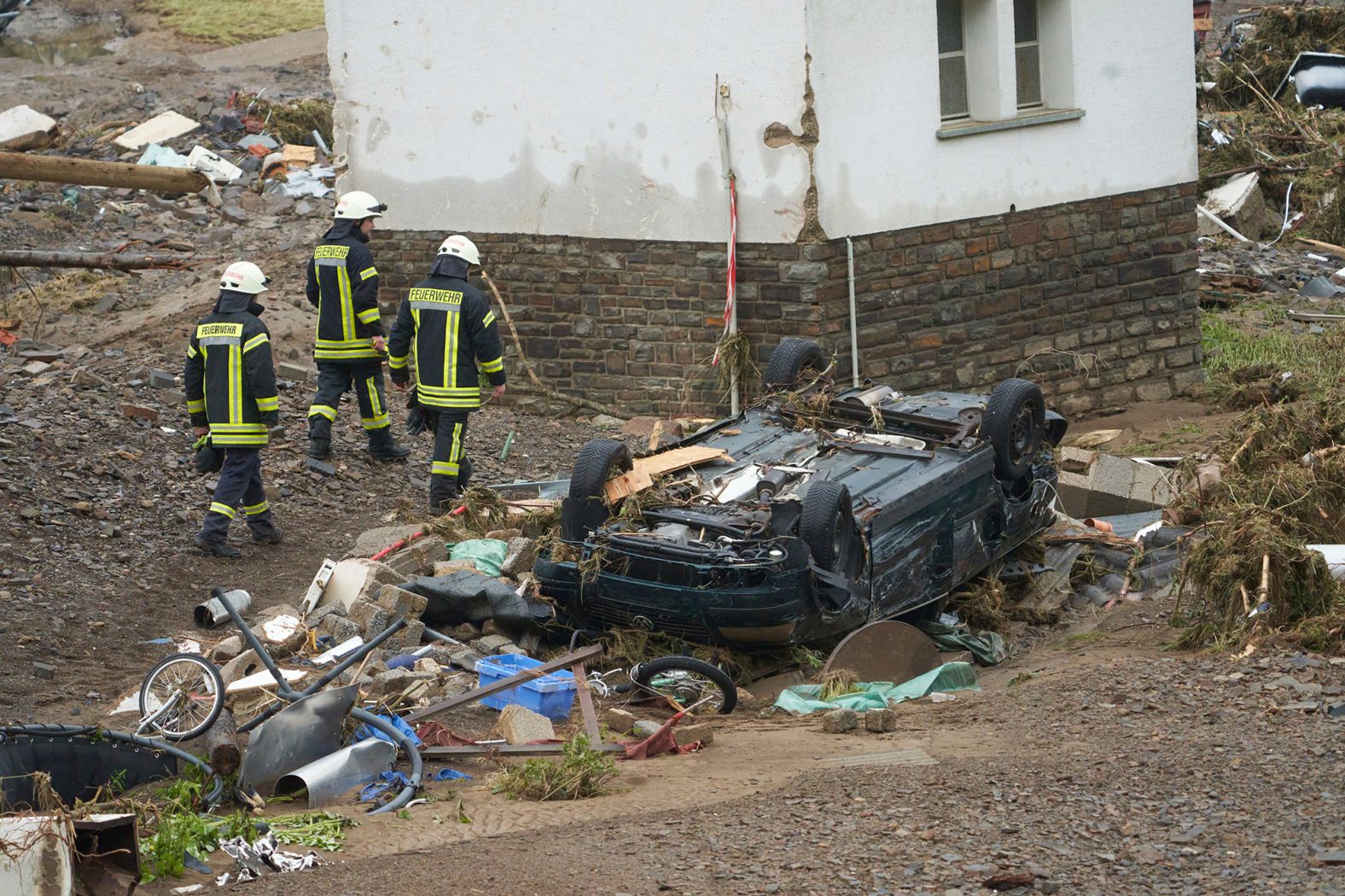 Firefighters walk past a car that was damaged by flooding in Schuld, Germany.