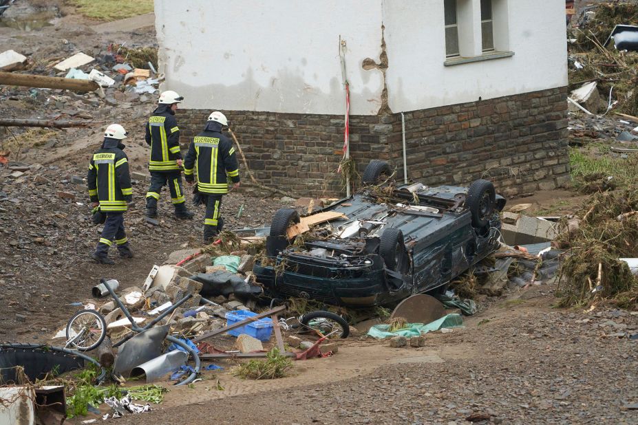 Firefighters walk past a car that was damaged by flooding in Schuld, Germany.
