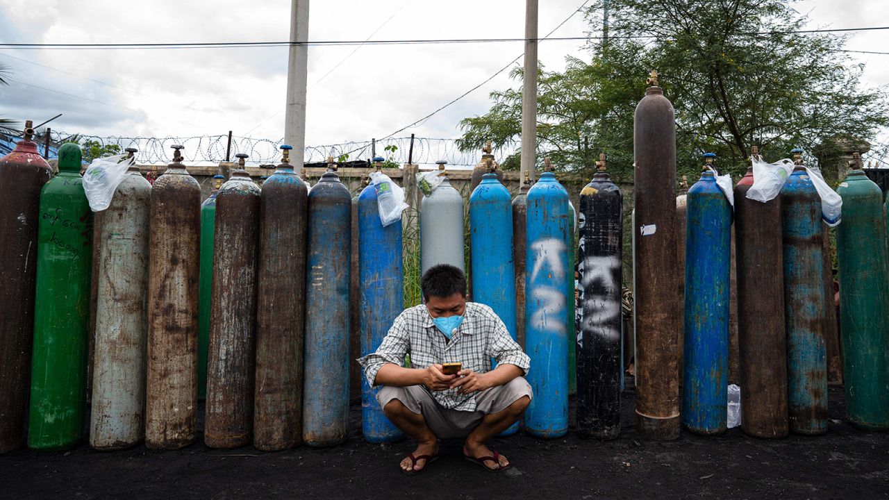 A man uses his mobile phone in front of empty oxygen canisters, which people are waiting to fill up, outside a factory in Mandalay, on July 13.