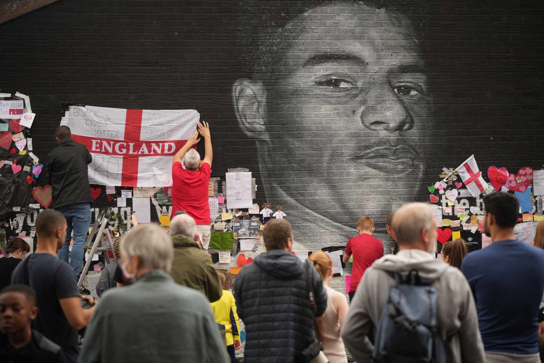 People look at the messages of support and the newly repaired mural of England footballer Marcus Rashford in Manchester, England.