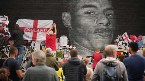 People look at the messages of support and the newly repaired mural of  Rashford, which is displayed on the wall of a cafe on Copson Street, Withington, after it was defaced by vandals.