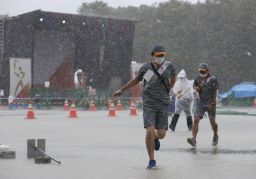 Staff members run to escape a rainstorm during an Olympic flame-lighting ceremony in Mizuho, western Tokyo, on July 11, 2021. 