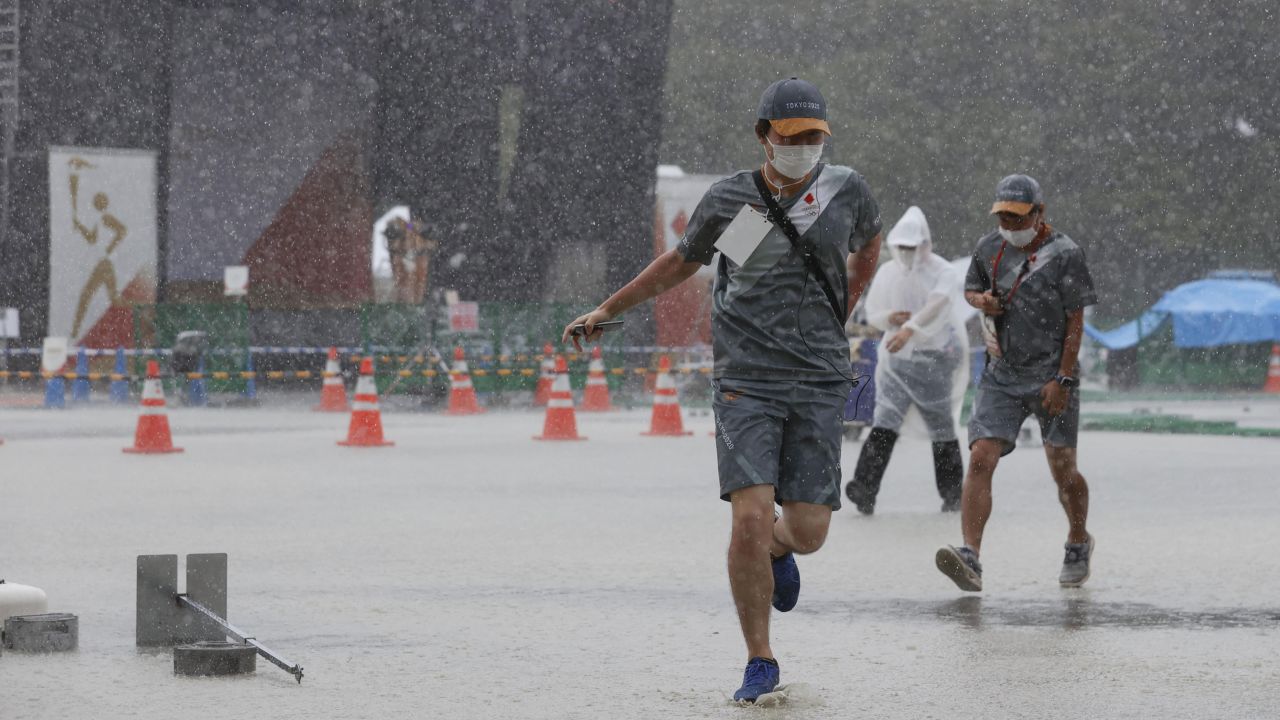 Staff members run to escape a rainstorm during an Olympic flame-lighting ceremony in Mizuho, western Tokyo, on July 11, 2021. 