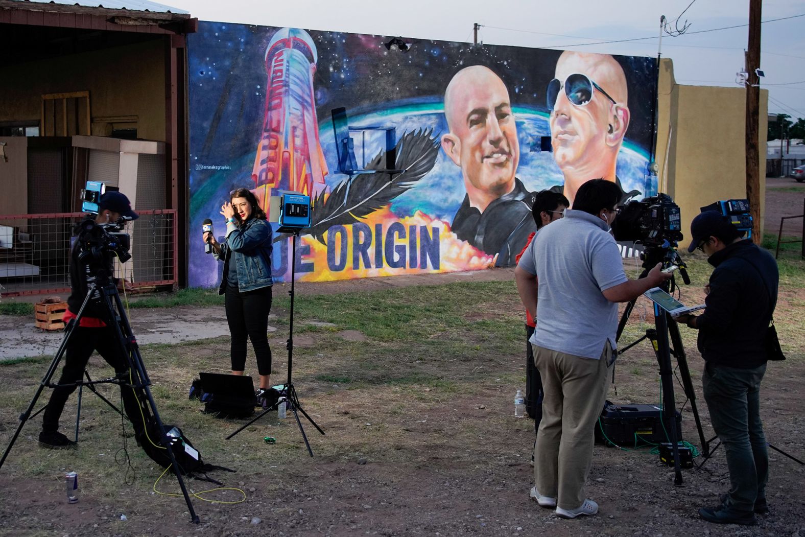 Reporter Celina Quintana Ortiz prepares to go live from Van Horn on Tuesday in front of a mural depicting Jeff and Mark Bezos.