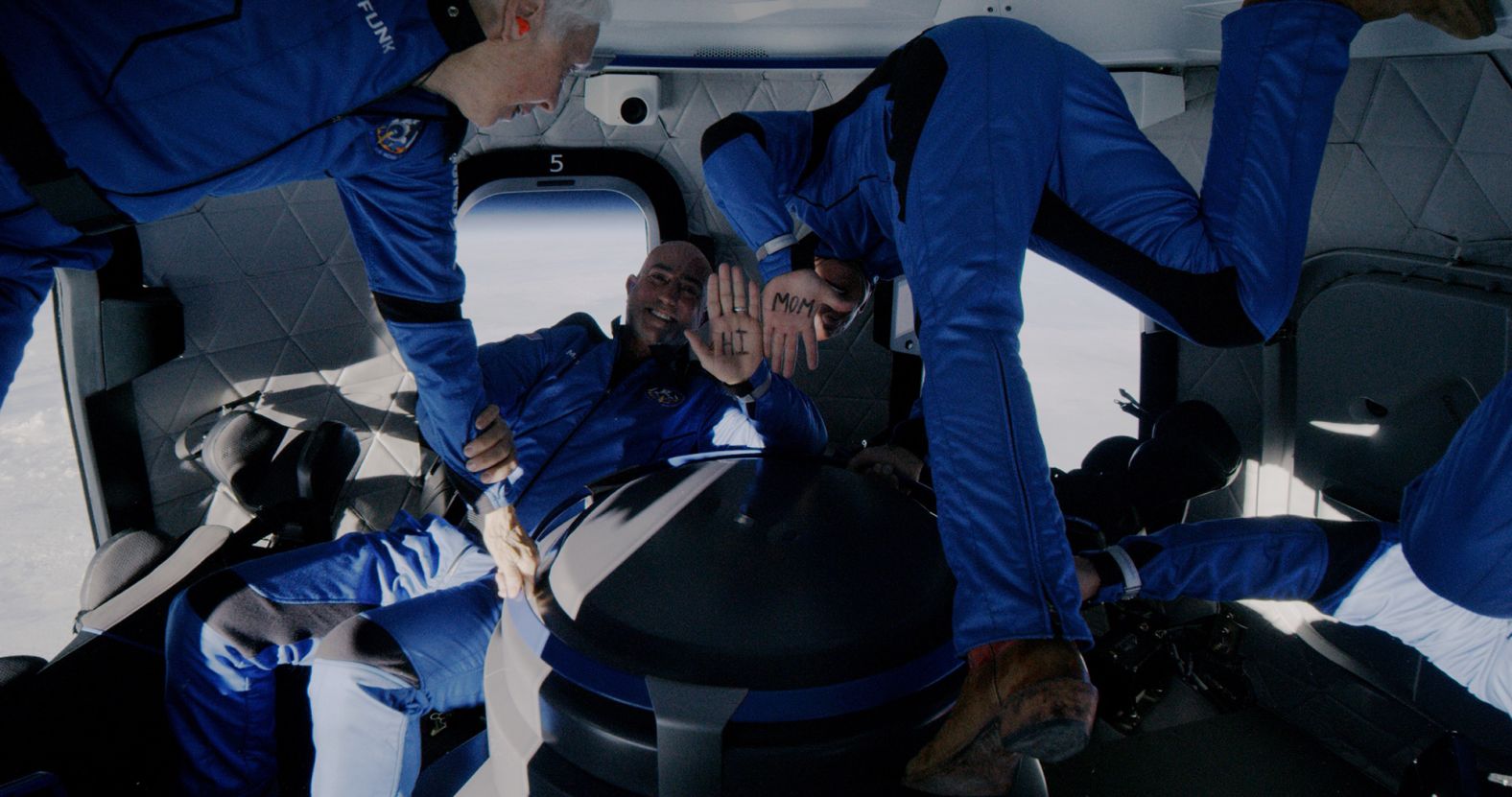 Mark and Jeff Bezos show "Hi Mom" written on their hands as the crew floats weightlessly in their capsule at the edge of space.