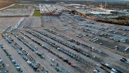 In this aerial photo, a General Motors assembly plant is seen at top right while mid-sized pickup trucks and full-size vans currently produced at the plant are seen in a parking lot outside Wednesday, March 24, 2021, in Wentzville, Mo. As the U.S. economy awakens from its pandemic-induced slumber, a vital cog is in short supply: the computer chips that power our cars and other vehicles, and a vast number of other items we take for granted.  Ford, GM and Stellantis have started building vehicles without some computers, putting them in storage with plans to retrofit them later. (AP Photo/Jeff Roberson)