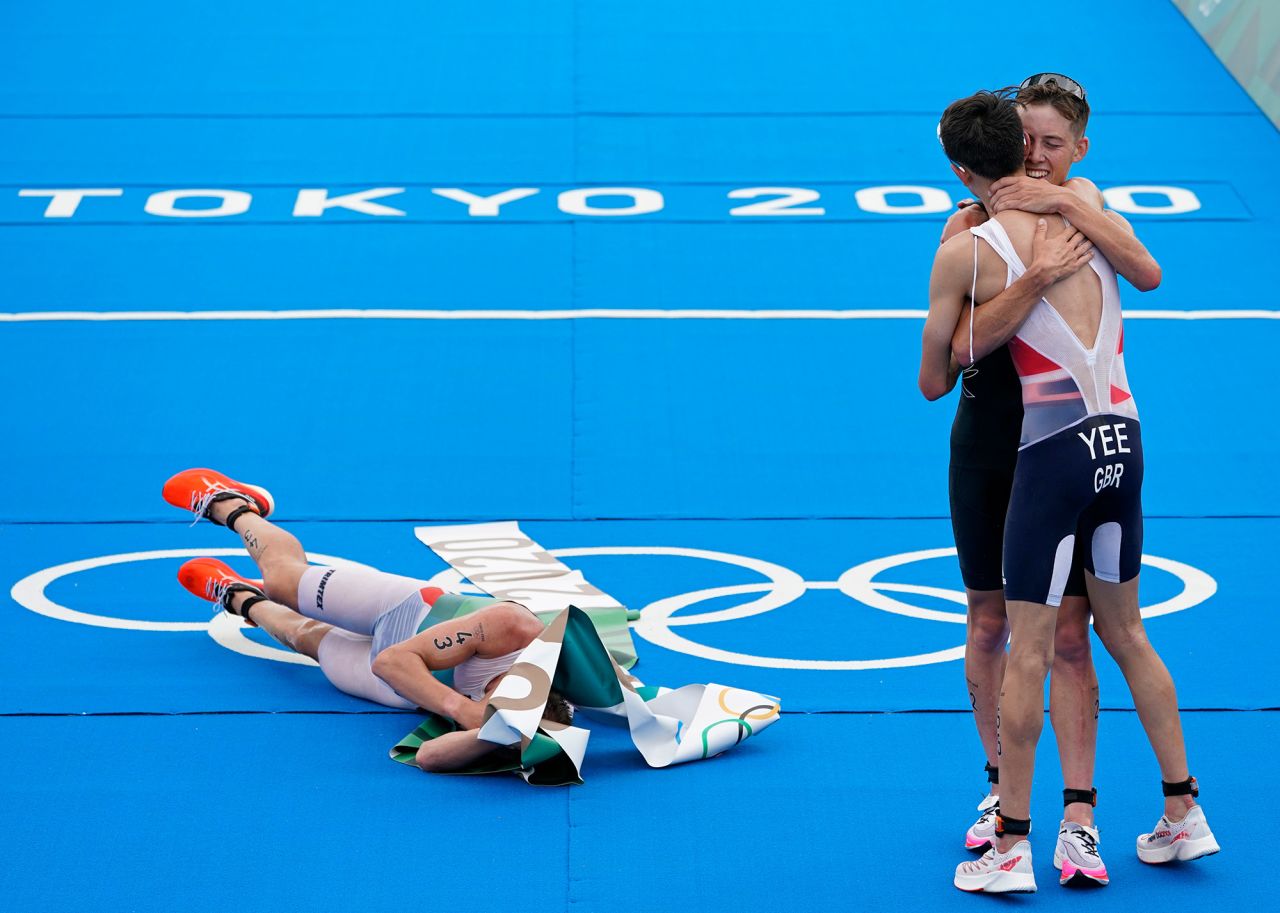 Norway's Kristian Blummenfelt lies on the ground wrapped in finish-line tape after he won the triathlon on July 26. On the right, silver medalist Alex Yee of Great Britain hugs bronze medalist Hayden Wilde of New Zealand.
