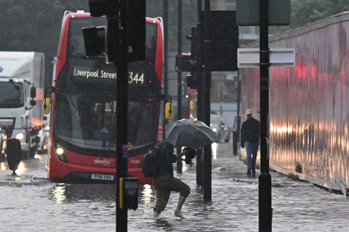 A pedestrian crosses through deep water on a flooded road in London on July 25, 2021.