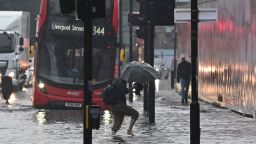 A pedestrian crosses through deep water on a flooded road in The Nine Elms district of London on July 25, 2021 during heavy rain. - Buses and cars were left stranded when roads across London flooded on Sunday, as repeated thunderstorms battered the British capital. (Photo by JUSTIN TALLIS / AFP) (Photo by JUSTIN TALLIS/AFP via Getty Images)