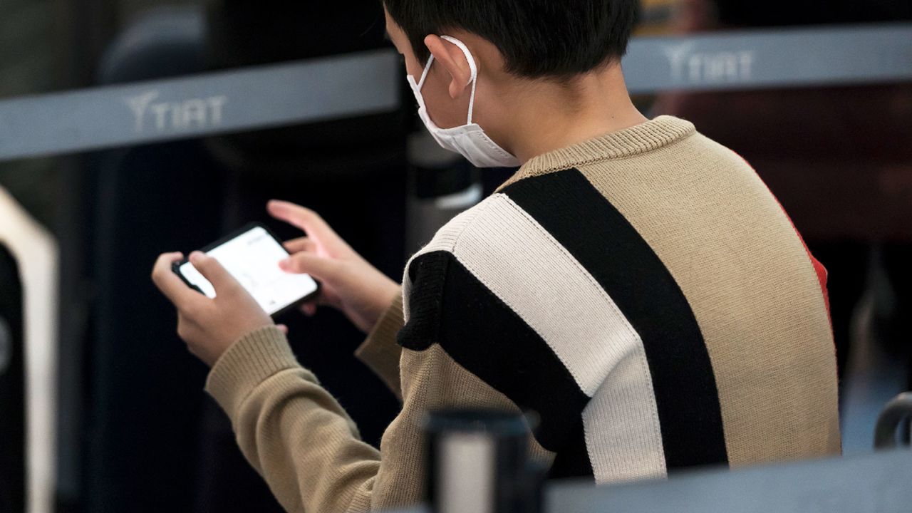 A boy plays a video game as he waits at Spring Airlines' check-in counter to take a flight bound for Wuhan at Haneda airport on January 31, 2020 in Tokyo, Japan. 