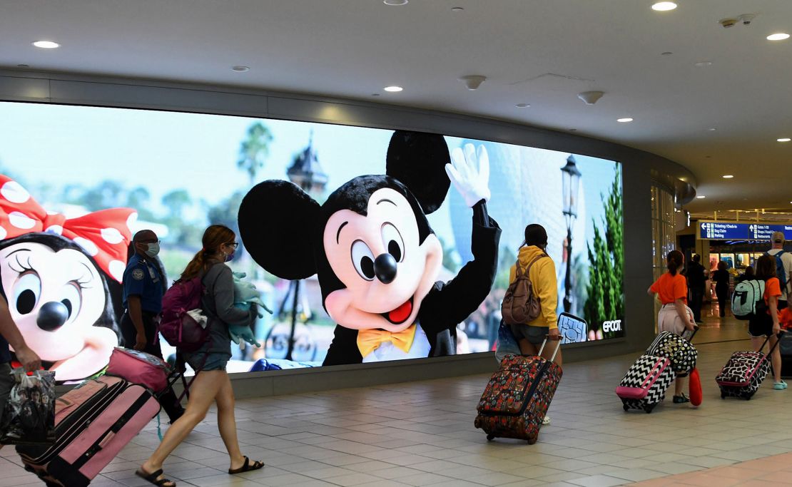 Travelers walk past a sign advertising Walt Disney World at Orlando International Airport as the July Fourth holiday weekend begins, on July 2, 2021.