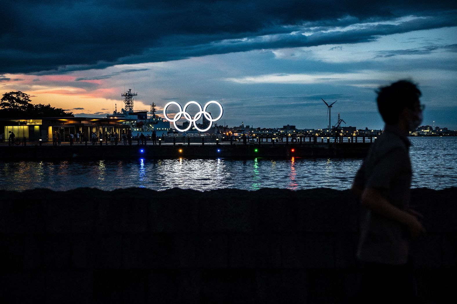 A man in Yokohama, Japan, walks past the Olympic rings lit up at dusk on July 27.