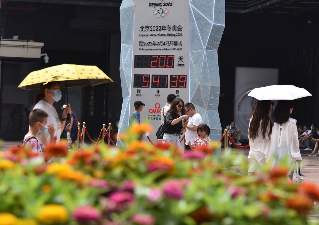 People wearing face masks walk past the countdown clock showing 200 days to the 2022 Olympic Winter Games.