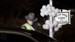White balloons decorate the sign for the Sandy Hook Elementary School as a Connecticut State Trooper stands guard at the school's entrance, Saturday, Dec. 15, 2012, in Newtown, Conn. A gunman killed his mother at their home and later walked into Sandy Hook Elementary School Friday and opened fire, killing 26 people, including 20 children. (AP Photo/David Goldman)