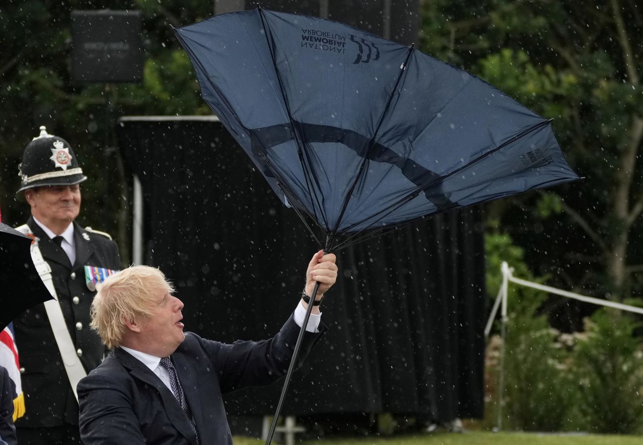 British Prime Minister Boris Johnson struggles with an umbrella during a visit to the National Memorial Arboretum in Alrewas, England, on Wednesday, July 28.