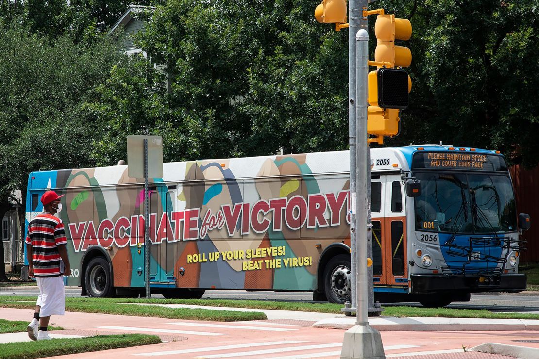 A masked man walks on July 20 in East Austin by a bus with a message advocating for people to get the coronavirus vaccine.