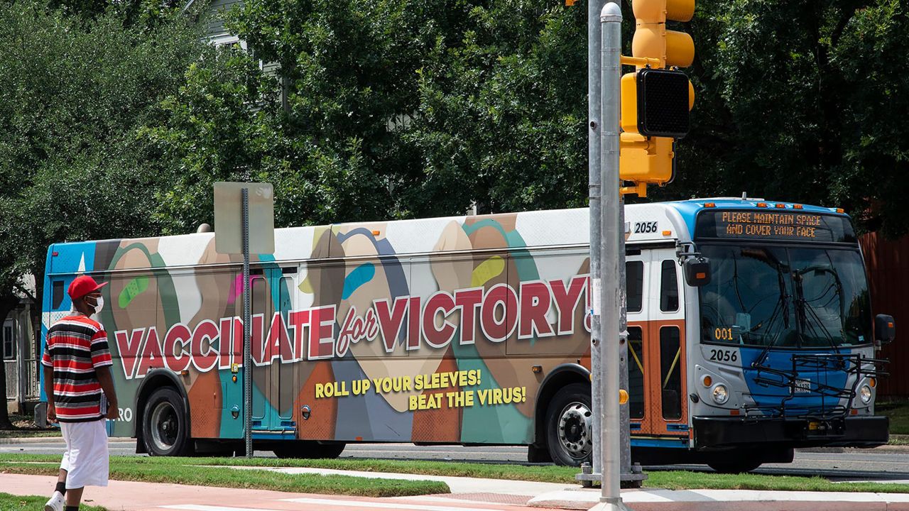 A masked man walks on July 20 in East Austin by a bus with a message advocating for people to get the coronavirus vaccine.