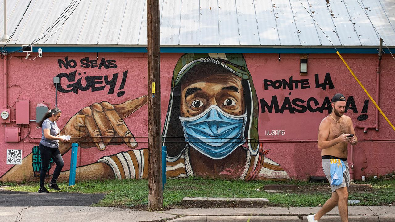 People pass a mural urging everyone to wear masks. The mural, seen on Tuesday, July 20, on Marcelino's restaurant in East Austin, translates to, "Don't be stupid. Put the mask on."
