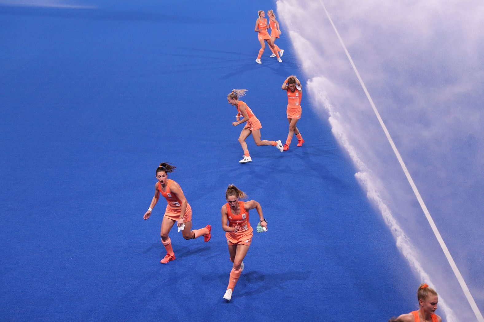 Dutch field hockey players run from sprinklers after pre-match warmups on July 31.