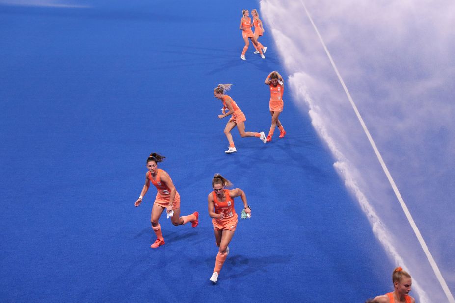 Dutch field hockey players run from sprinklers after pre-match warmups on July 31.