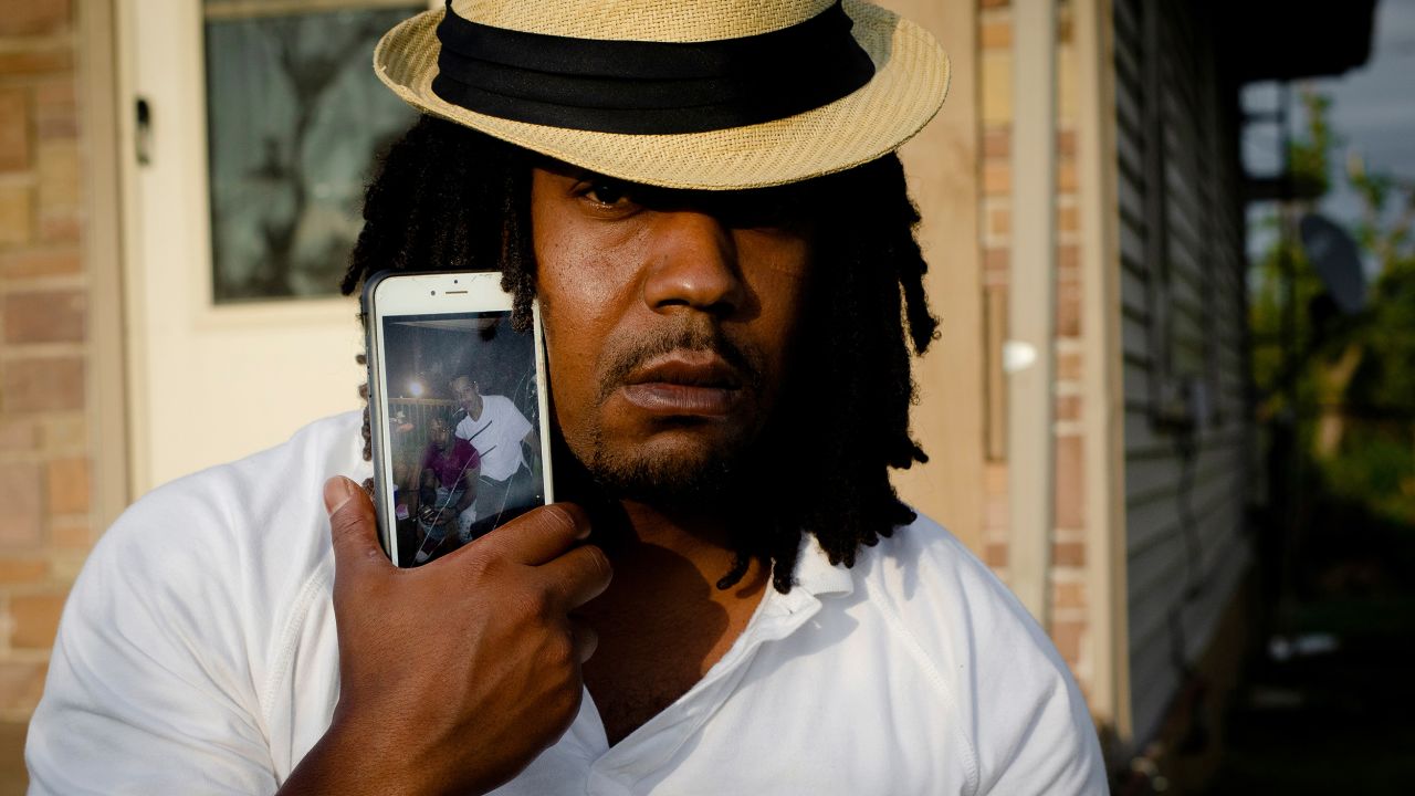 Dion Green holds a cell phone showing a picture of himself and his father, Derrick Fudge.